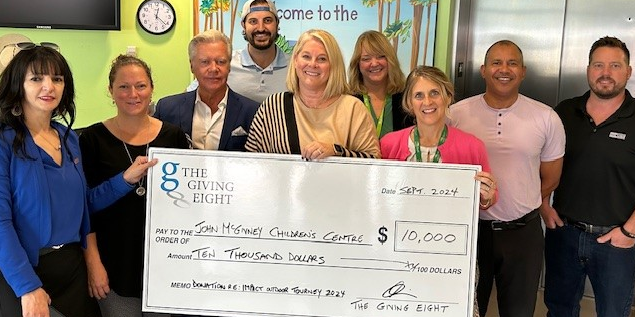 group photo of Giving 8 volunteers with JMCC staff accepting a cheque for $10,000