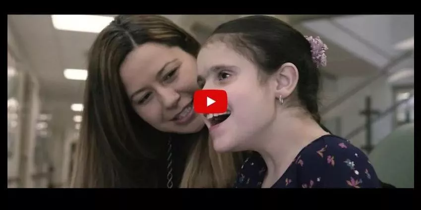 A woman smiles at a young girl speaking in an indoor hallway setting.