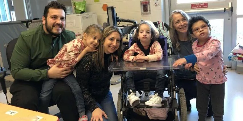 Five people, including children and adults, with one child in a wheelchair in an indoor setting.