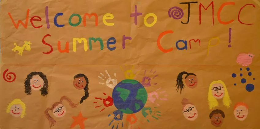 Colorful poster on brown paper welcoming to JMCC Summer Camp with diverse faces and handprints.