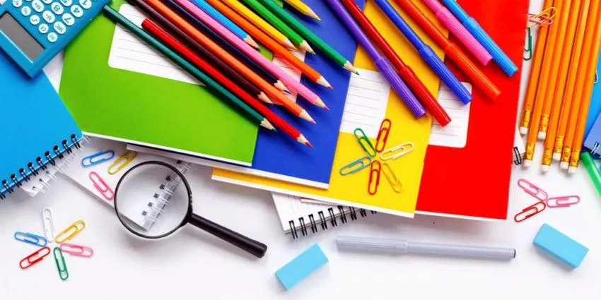 Colorful school supplies including notebooks, pencils, crayons, paper clips, magnifying glass, calculator, and erasers on white surface