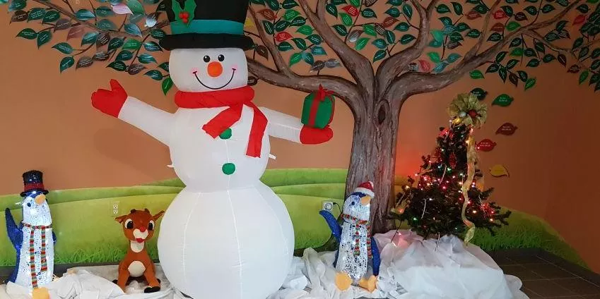 Inflatable snowman with gift, two penguins, plush reindeer, and decorated Christmas tree.