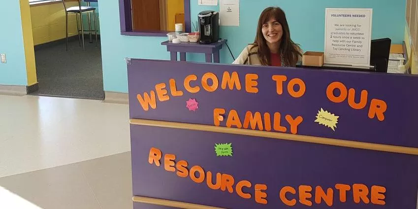 Woman seated behind a purple desk with welcome message at family resource center reception.