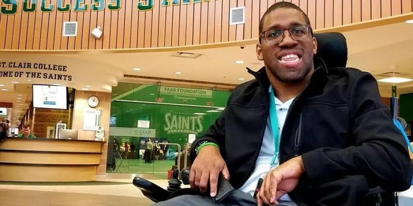 Man in wheelchair inside St. Clair College with signage for Saints and reception area.