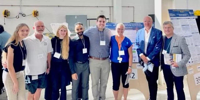 Group of nine people standing indoors in front of display boards at a conference.