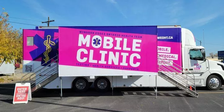 Mobile clinic vehicle with pink signage offering health testing and services with stair entry ramps.