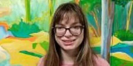 Young woman with glasses and long brown hair smiling in front of a colorful abstract painting background