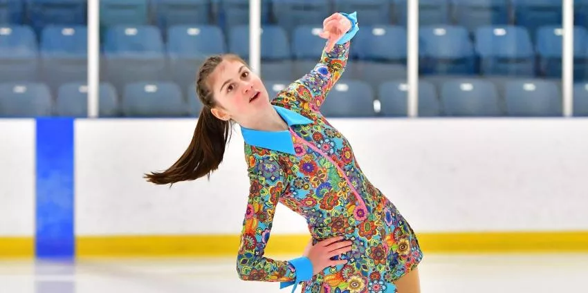 Female figure skater performing on ice wearing a colorful floral costume with blue accents.