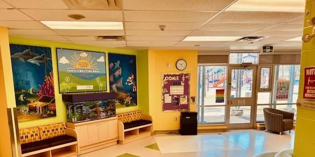 Waiting area with aquatic murals, patterned benches, fish tank, bulletin board, clock, and glass door to playground.