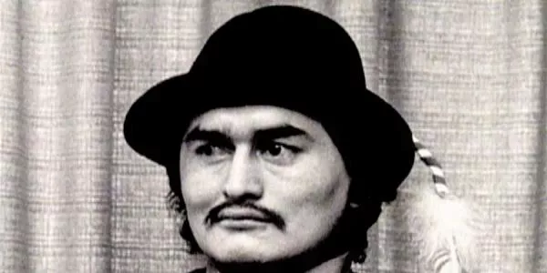 Black and white photo of a man with a bowler hat and mustache in front of curtains