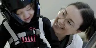 Woman wearing glasses smiles at child in helmet and safety harness.
