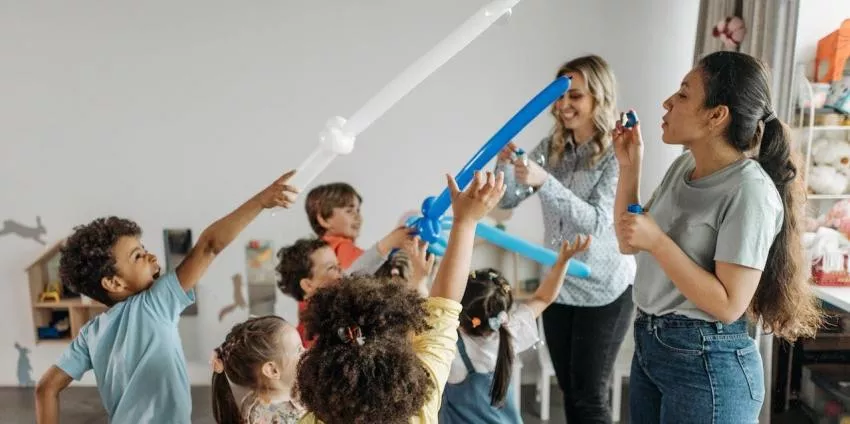 Children playing with balloon swords while two adults supervise and engage in a room.