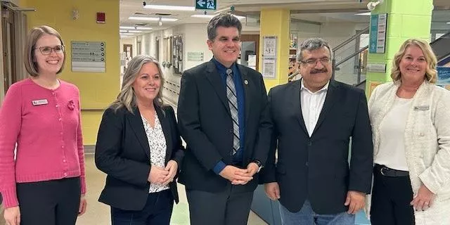 Five professionally dressed individuals standing together in a hallway posing for a group photo