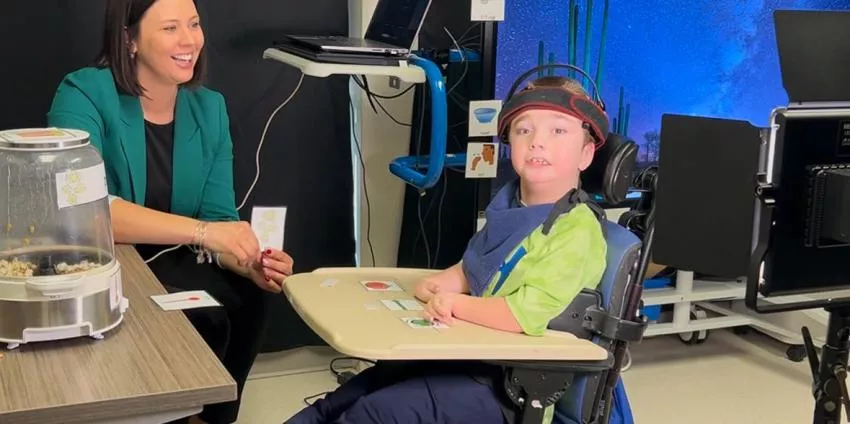 Child in wheelchair playing a card game with an adult woman in a therapy room.