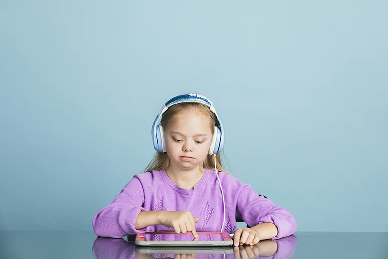 Girl with Down Syndrome using a digital tablet with headphones