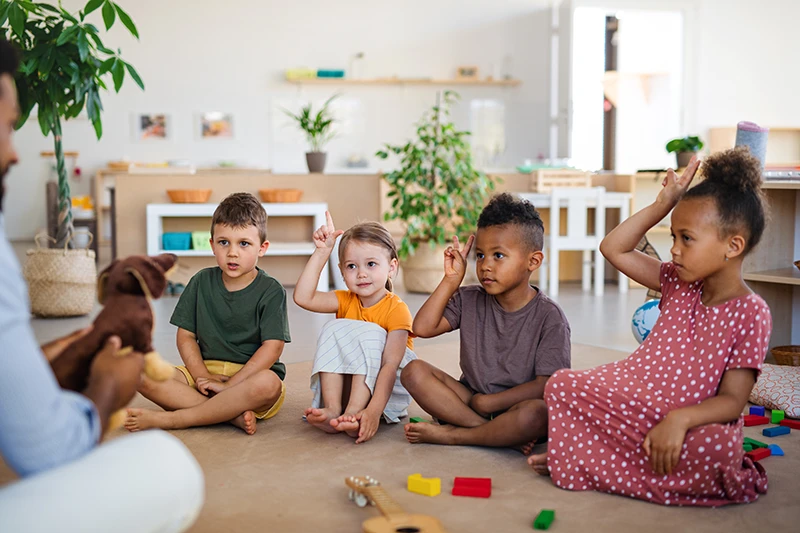 Group of nursery school children with teacher sitting on the classroom floor
