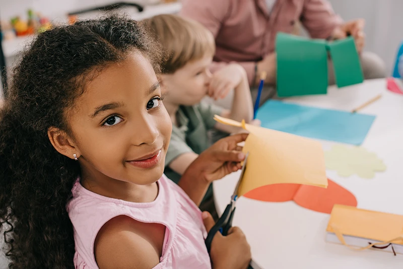 Preschooler cutting colourful paper in classroom