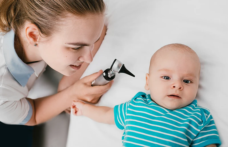 Smiling pediatrician doing ear exam with an otoscope to a baby