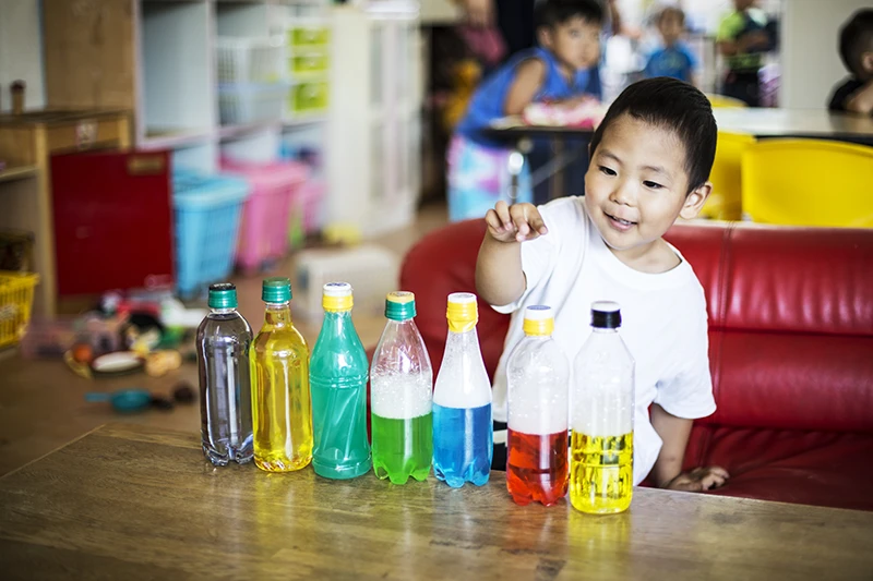 Young boy playing with colourful bottles of liquid at preschool