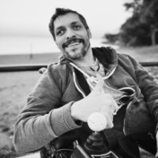 Man in a motorized wheelchair outdoors giving a thumbs-up with a golf ball joystick in black and white.