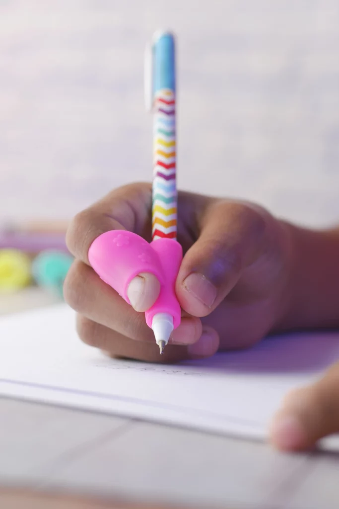 Hand holding a colorful chevron pen with pink grip writing on paper close-up