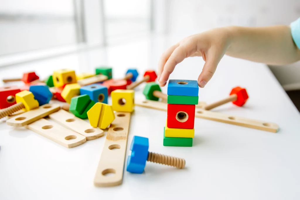 Child's hand stacking colorful wooden blocks with construction pieces on white table