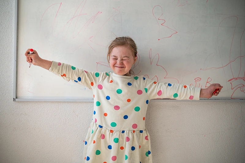 Happy little girl with down syndrome standing in front of whiteboard