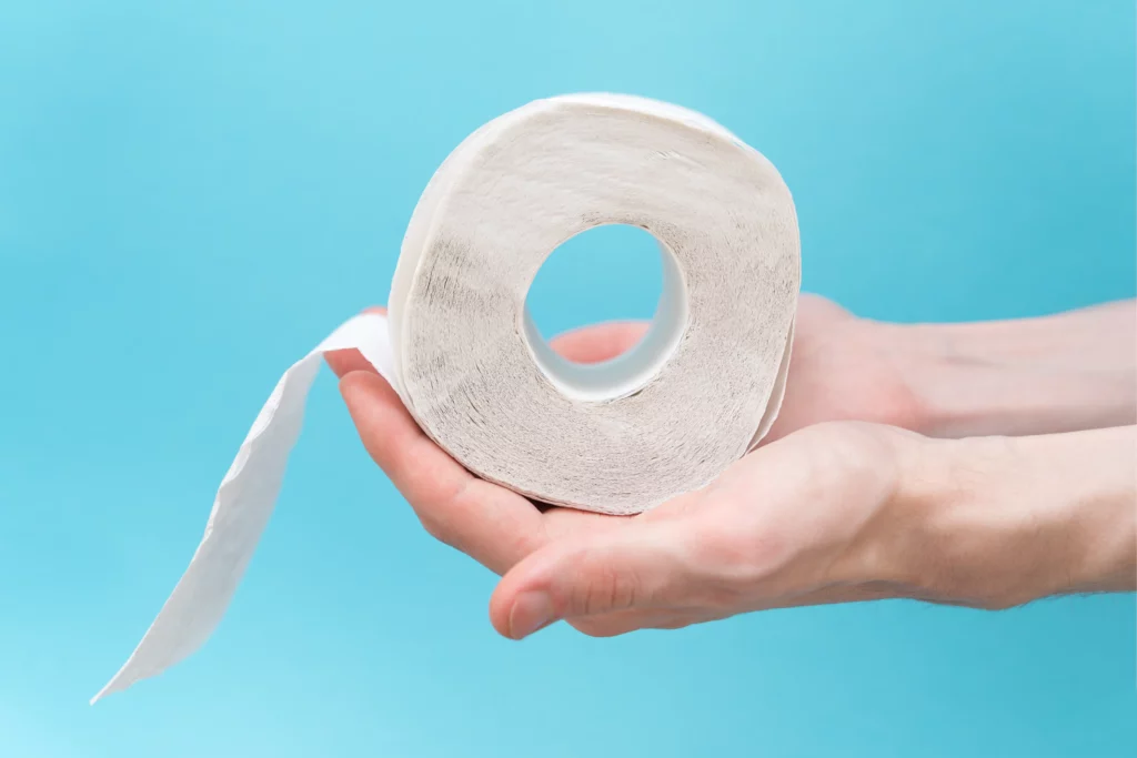 Hands holding a partially unrolled toilet paper roll against a blue background