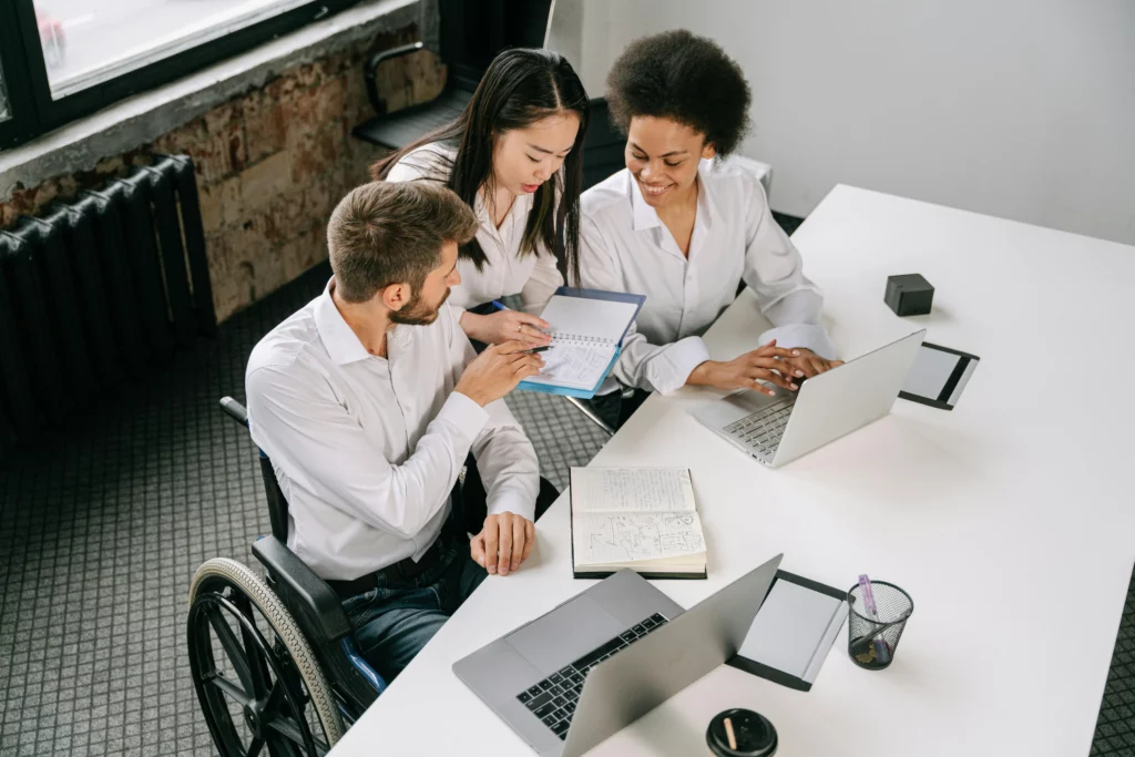 Three colleagues working together at a table with laptops and notebooks in an office.